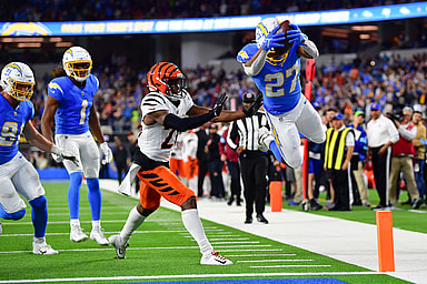 Nov 17, 2024; Inglewood, California, USA; Los Angeles Chargers running back J.K. Dobbins (27) scores a touchdown ahead of cornerback Josh Newton (28) during the second half at SoFi Stadium. Mandatory Credit: Gary A. Vasquez-Imagn Images
