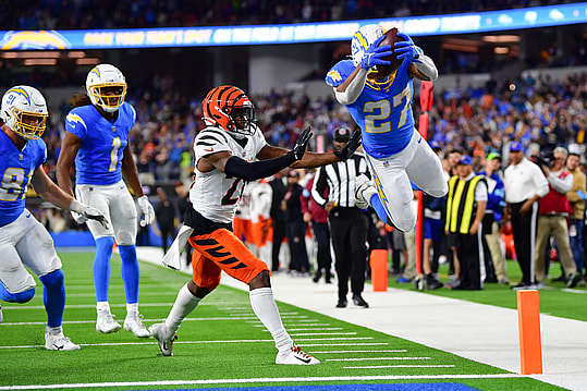 Nov 17, 2024; Inglewood, California, USA; Los Angeles Chargers running back J.K. Dobbins (27) scores a touchdown ahead of cornerback Josh Newton (28) during the second half at SoFi Stadium. Mandatory Credit: Gary A. Vasquez-Imagn Images