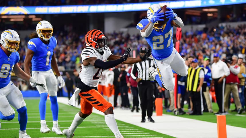 Nov 17, 2024; Inglewood, California, USA; Los Angeles Chargers running back J.K. Dobbins (27) scores a touchdown ahead of cornerback Josh Newton (28) during the second half at SoFi Stadium. Mandatory Credit: Gary A. Vasquez-Imagn Images