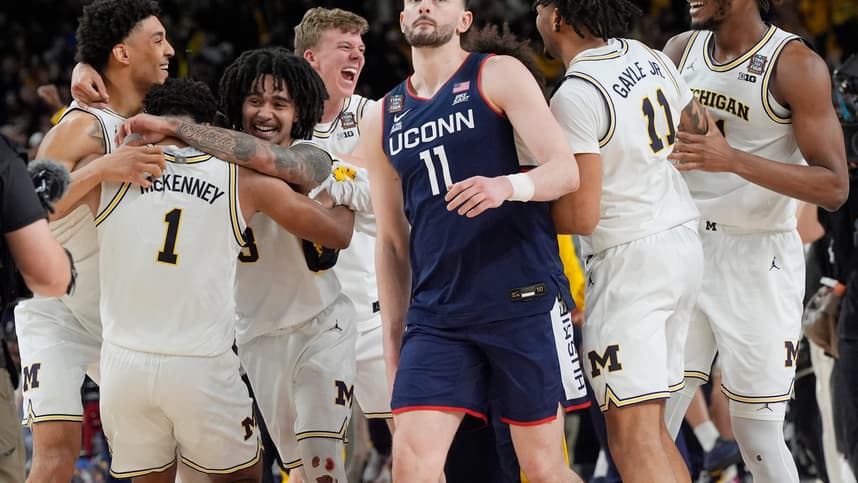 Michigan basketball celebrates winning the NCAA national championship, 69-63, as Connecticut forward Alex Karaban (11) walks off
