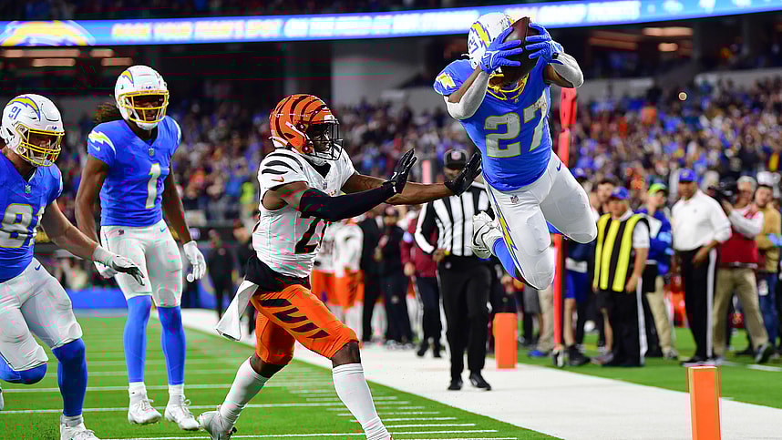 Nov 17, 2024; Inglewood, California, USA; Los Angeles Chargers running back J.K. Dobbins (27) scores a touchdown ahead of cornerback Josh Newton (28) during the second half at SoFi Stadium. Mandatory Credit: Gary A. Vasquez-Imagn Images