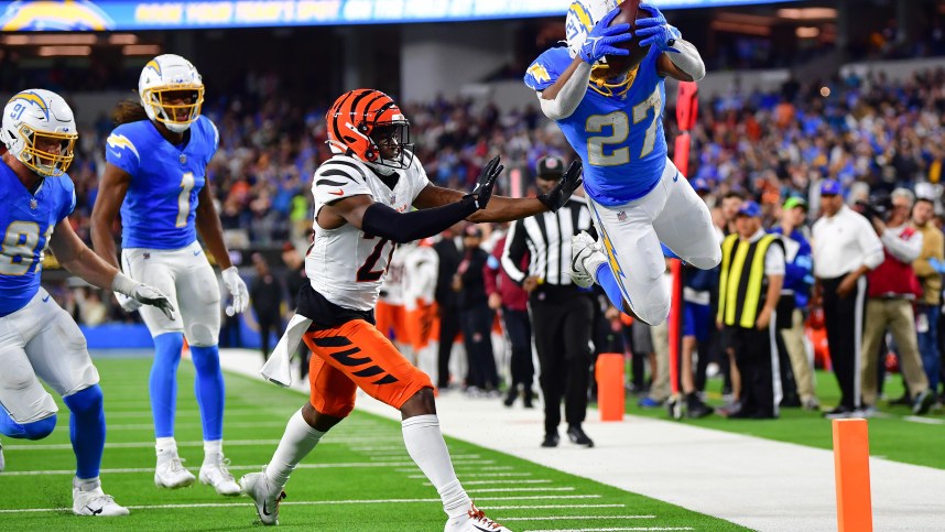 Nov 17, 2024; Inglewood, California, USA; Los Angeles Chargers running back J.K. Dobbins (27) scores a touchdown ahead of cornerback Josh Newton (28) during the second half at SoFi Stadium. Mandatory Credit: Gary A. Vasquez-Imagn Images