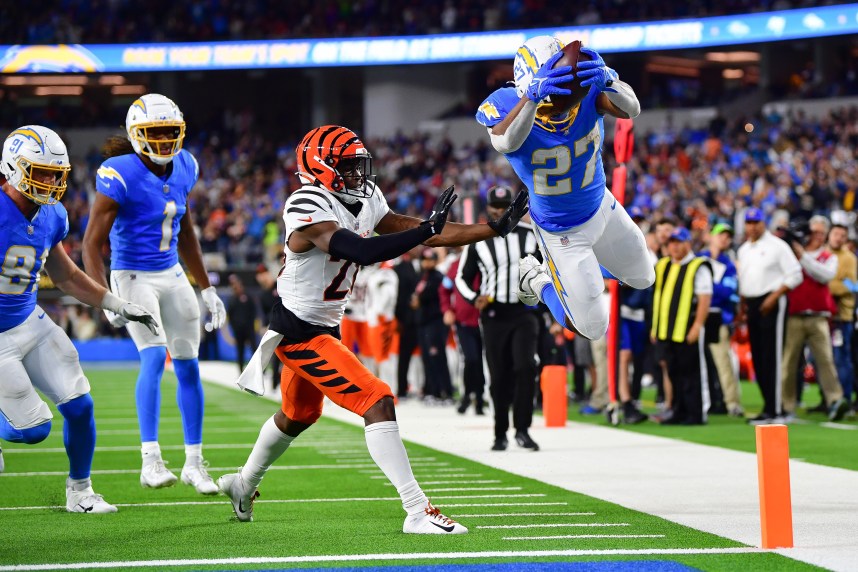 Nov 17, 2024; Inglewood, California, USA; Los Angeles Chargers running back J.K. Dobbins (27) scores a touchdown ahead of cornerback Josh Newton (28) during the second half at SoFi Stadium. Mandatory Credit: Gary A. Vasquez-Imagn Images