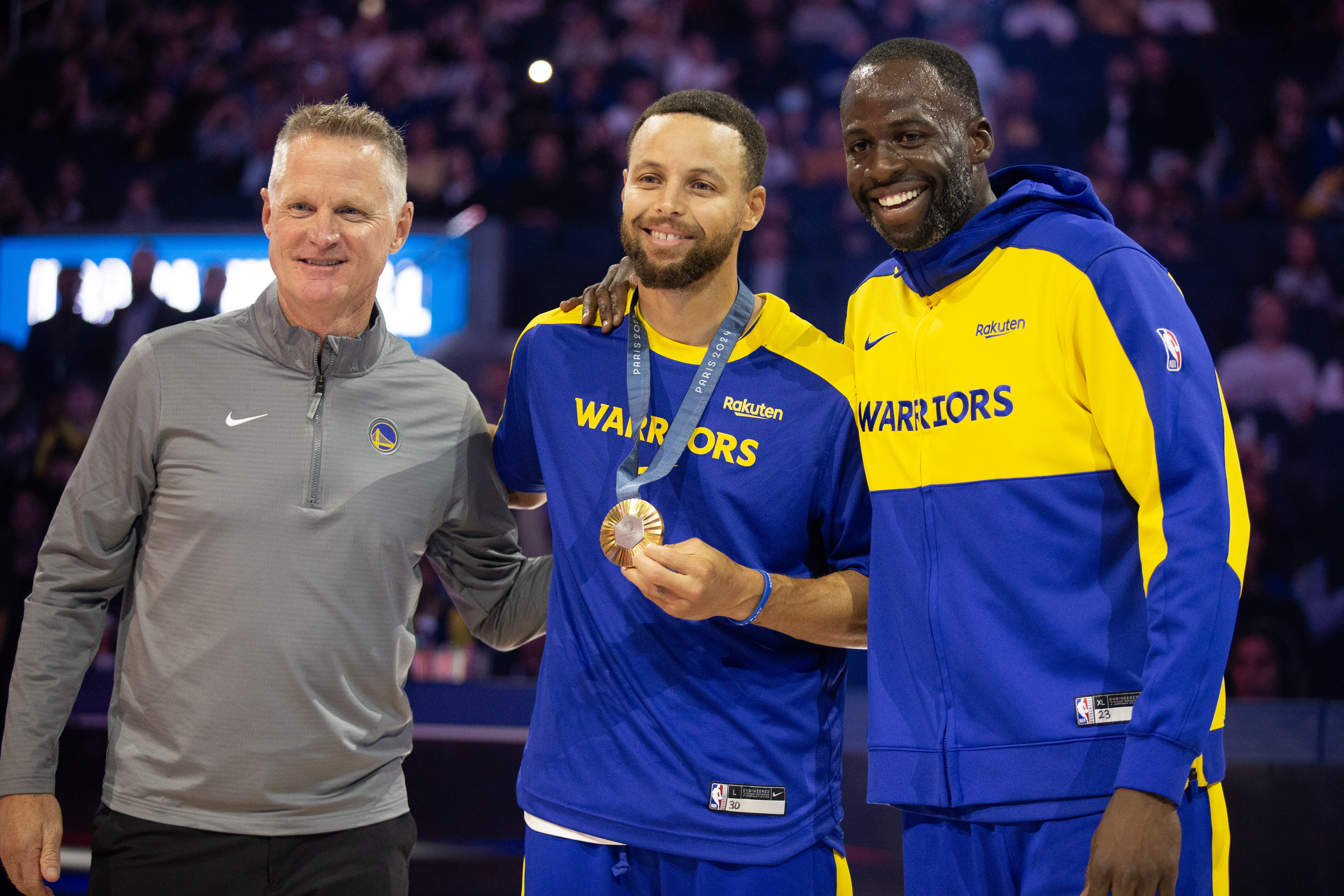 Oct 11, 2024; San Francisco, California, USA; Golden State Warriors guard Stephen Curry (center) is flanked by head coach Steve Kerr and forward Draymond Green as he is presented his gold medal for his performance for Team USA at the 2024 Summer Olympics in Paris before taking on the Sacramento Kings at Chase Center. Mandatory Credit: D. Ross Cameron-Imagn Images